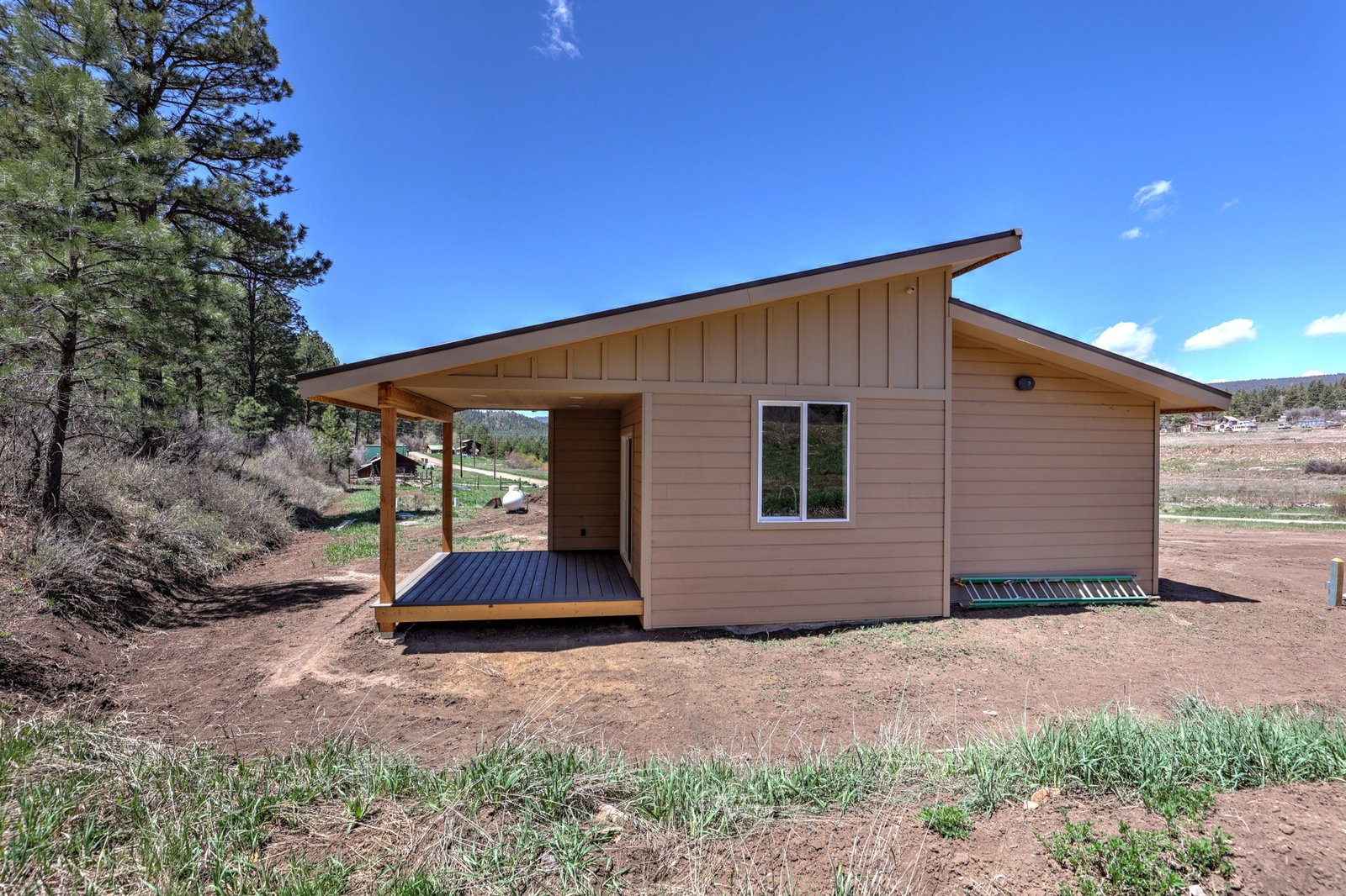 A newly completed custom home with a covered porch, set against pines and blue Colorado sky